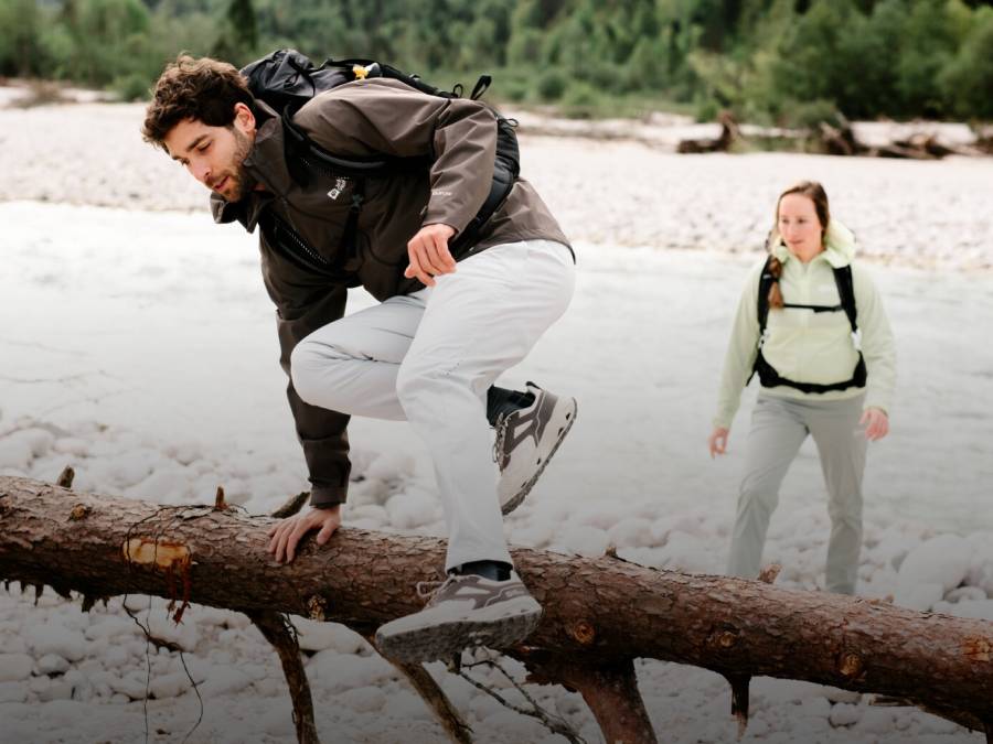 Young man in hiking clothes jumps over a tree trunk